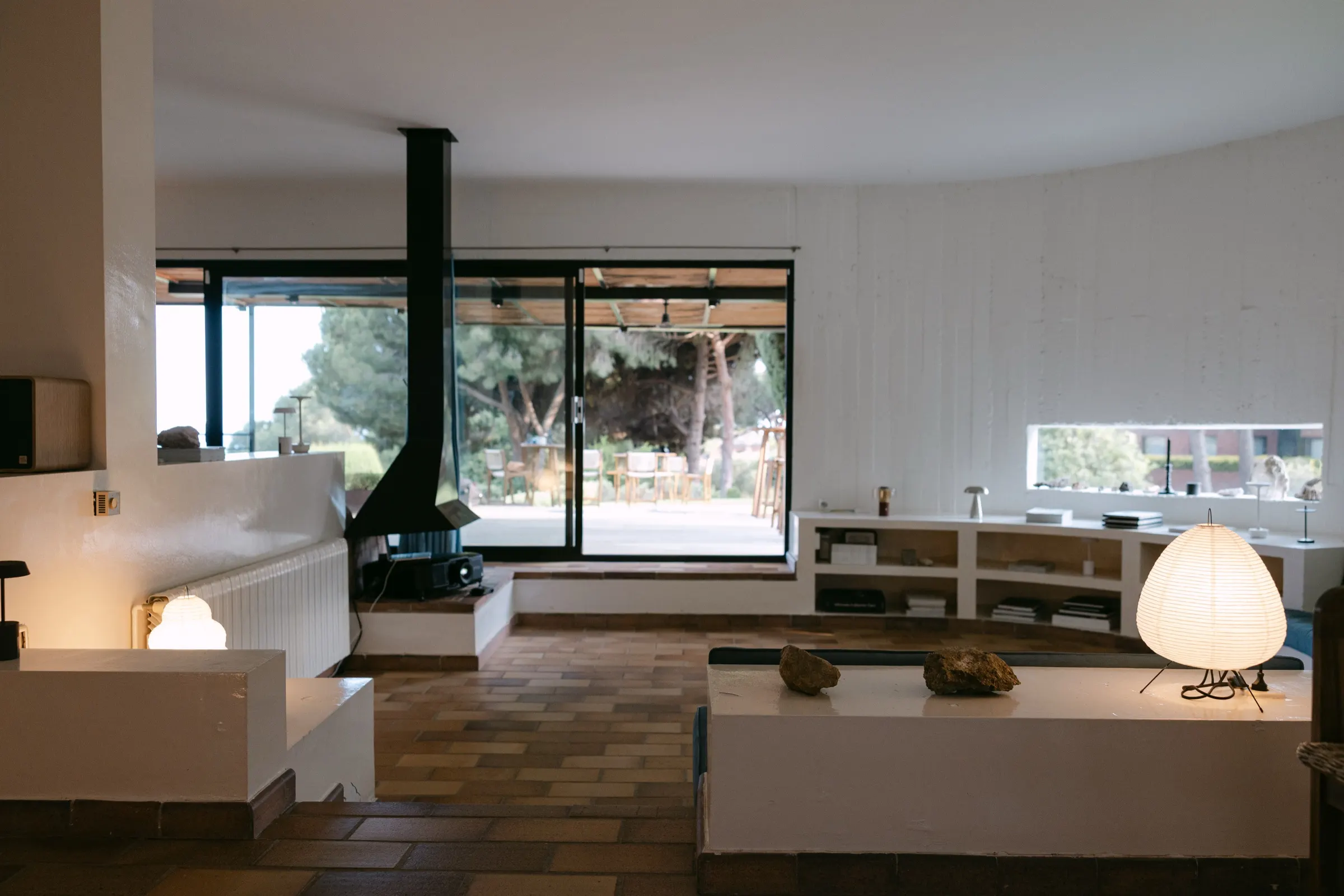 Salón de la Casa Semienterrada con chimenea suspendida y lámparas de papel en el evento AD100. Fotografía de Noomadik.