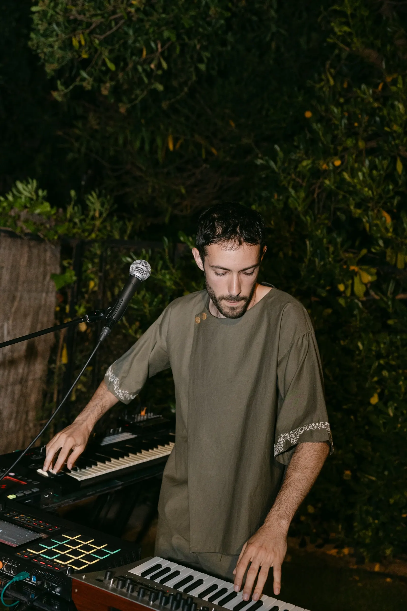 Músico con teclados y sintetizadores tocando de noche en el jardín de la fiesta AD100. Fotografía de Noomadik.