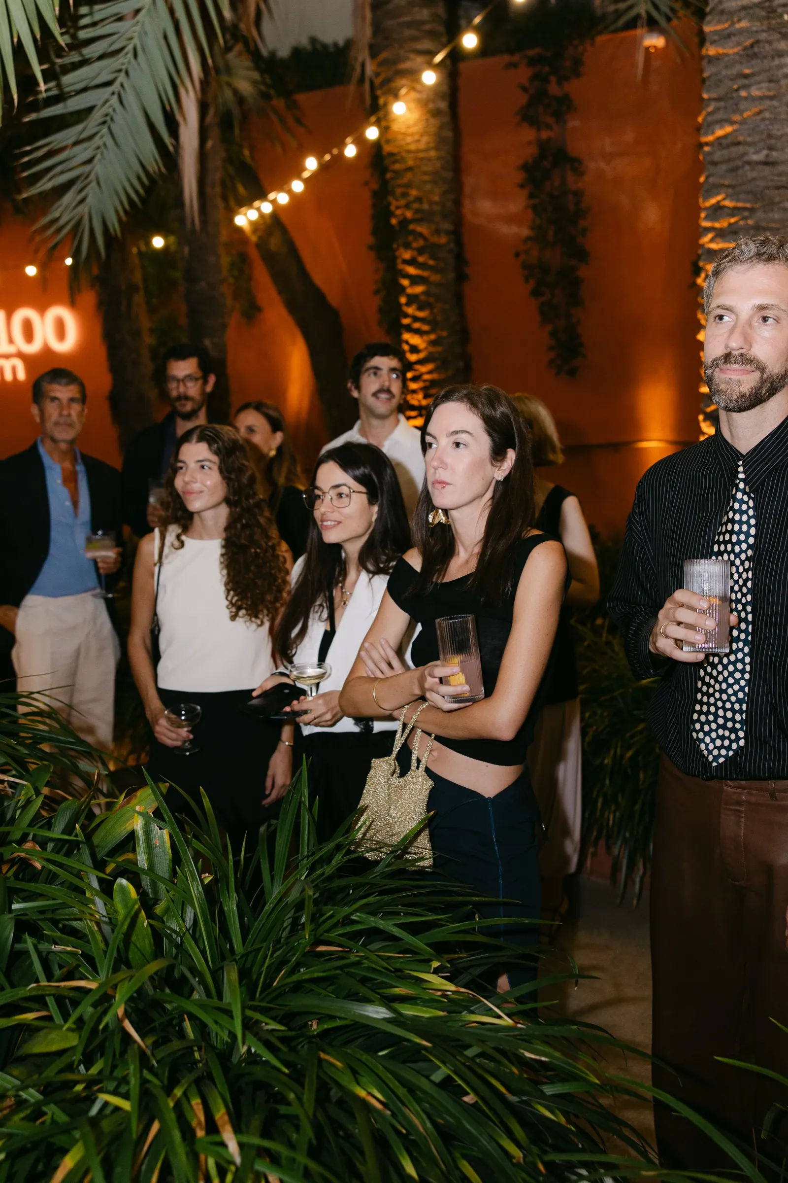 Grupo de invitados con copas entre plantas y guirnaldas de luz en el AD100 de Casa Vicens. Fotografía de Noomadik.