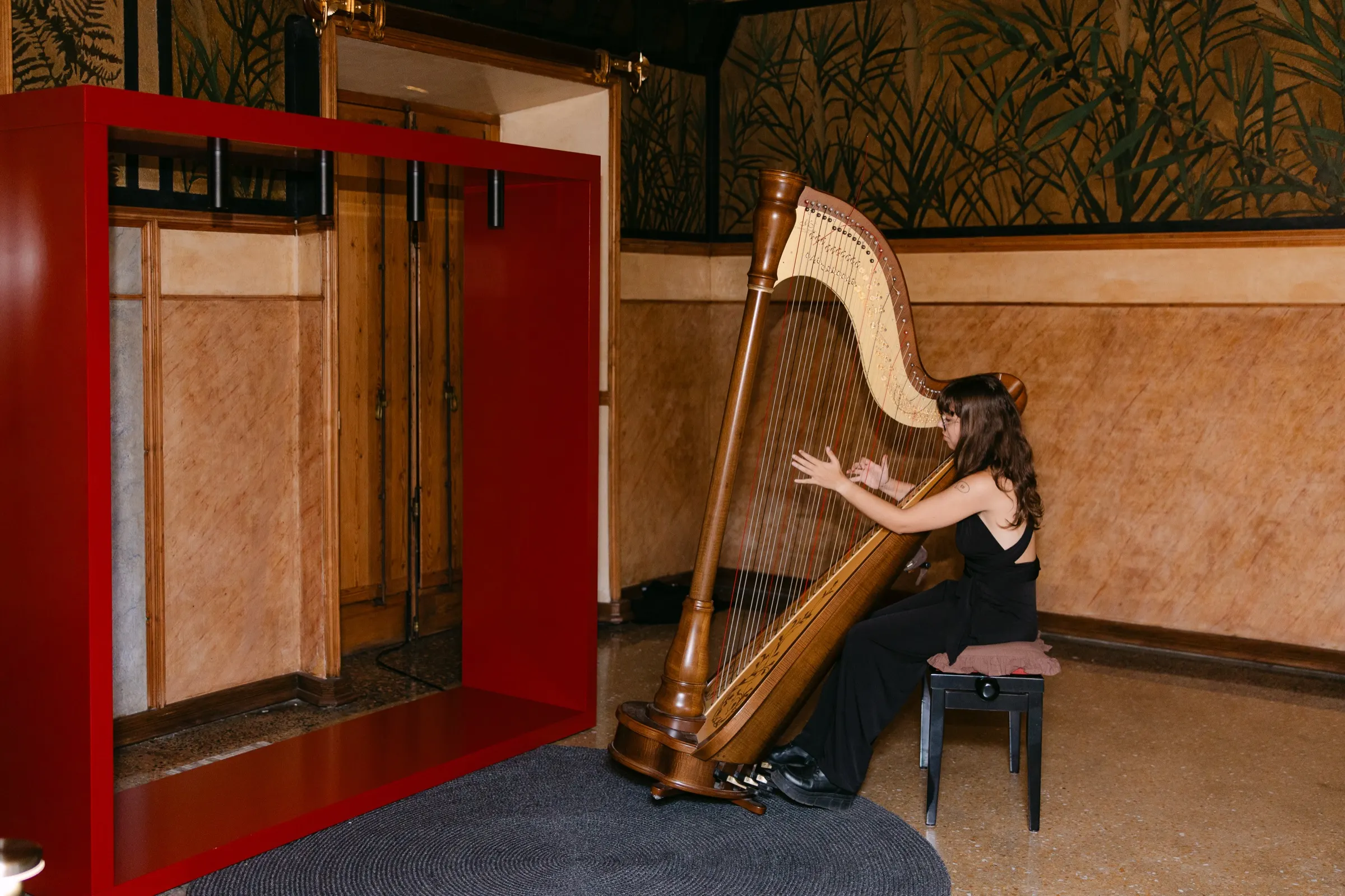 Arpista tocando junto a una estructura roja en un salón de la Casa Vicens durante el AD100. Fotografía de Noomadik.
