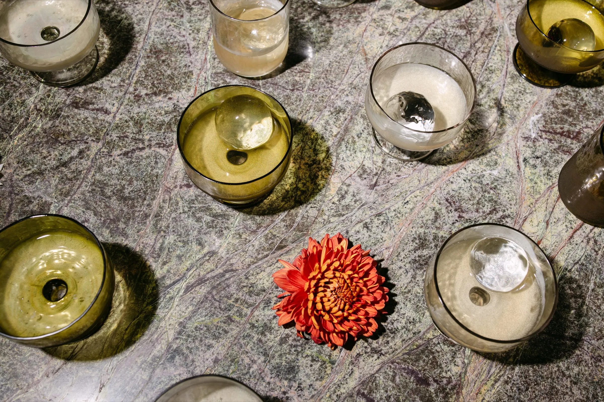 Copas de vidrio verde y una flor naranja sobre una mesa de mármol en el AD100. Fotografía de Noomadik.