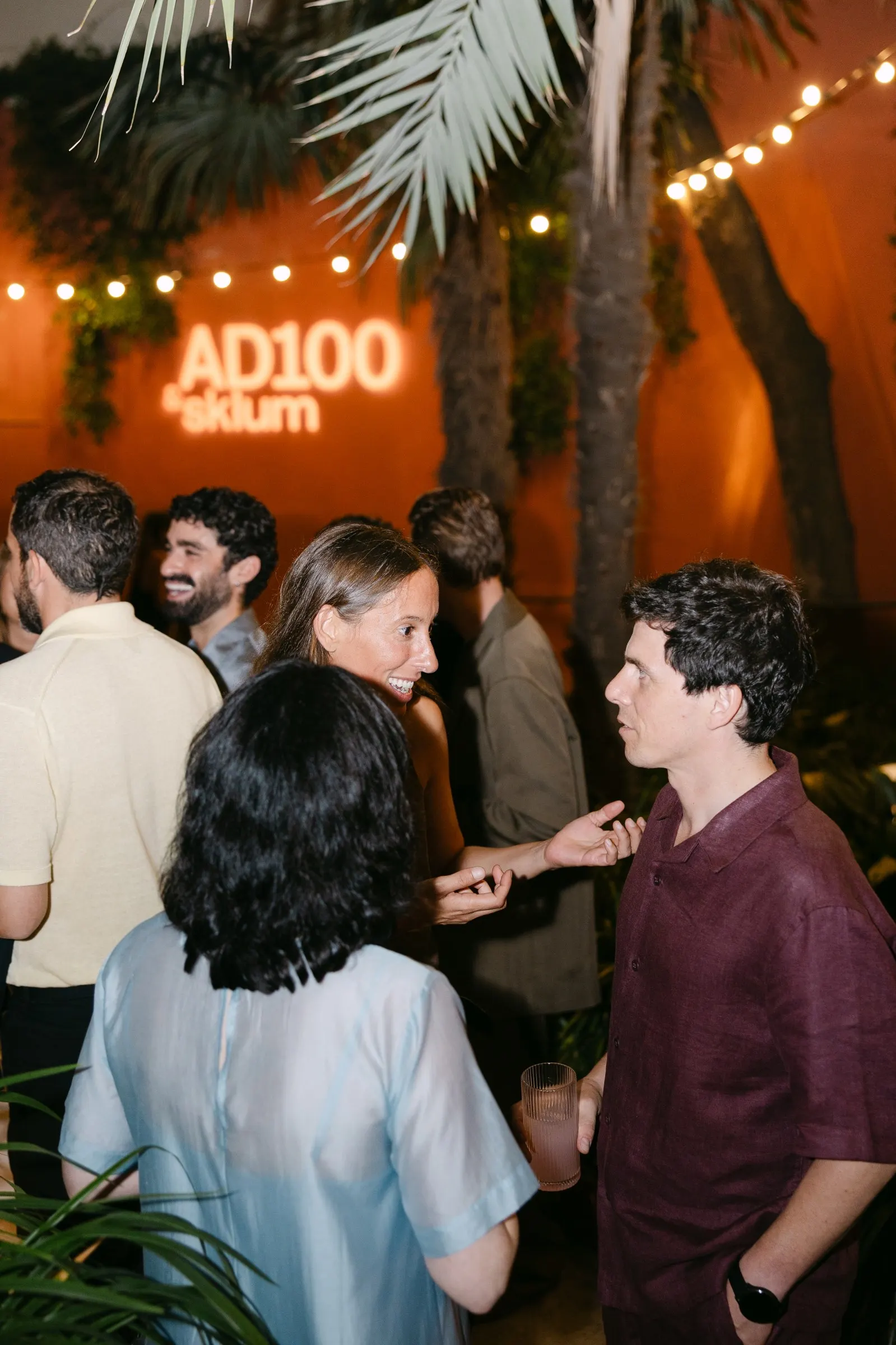 Convidats conversant sota el rètol lluminós AD100 × Sklum a la Casa Vicens. Fotografia de Noomadik.
