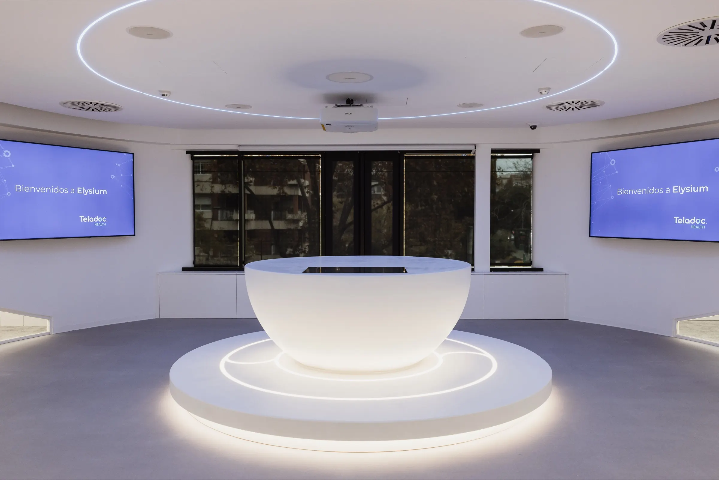 Sala circular blanca con mostrador iluminado en las oficinas de Teladoc Health en Barcelona. Fotografía de Noomadik.
