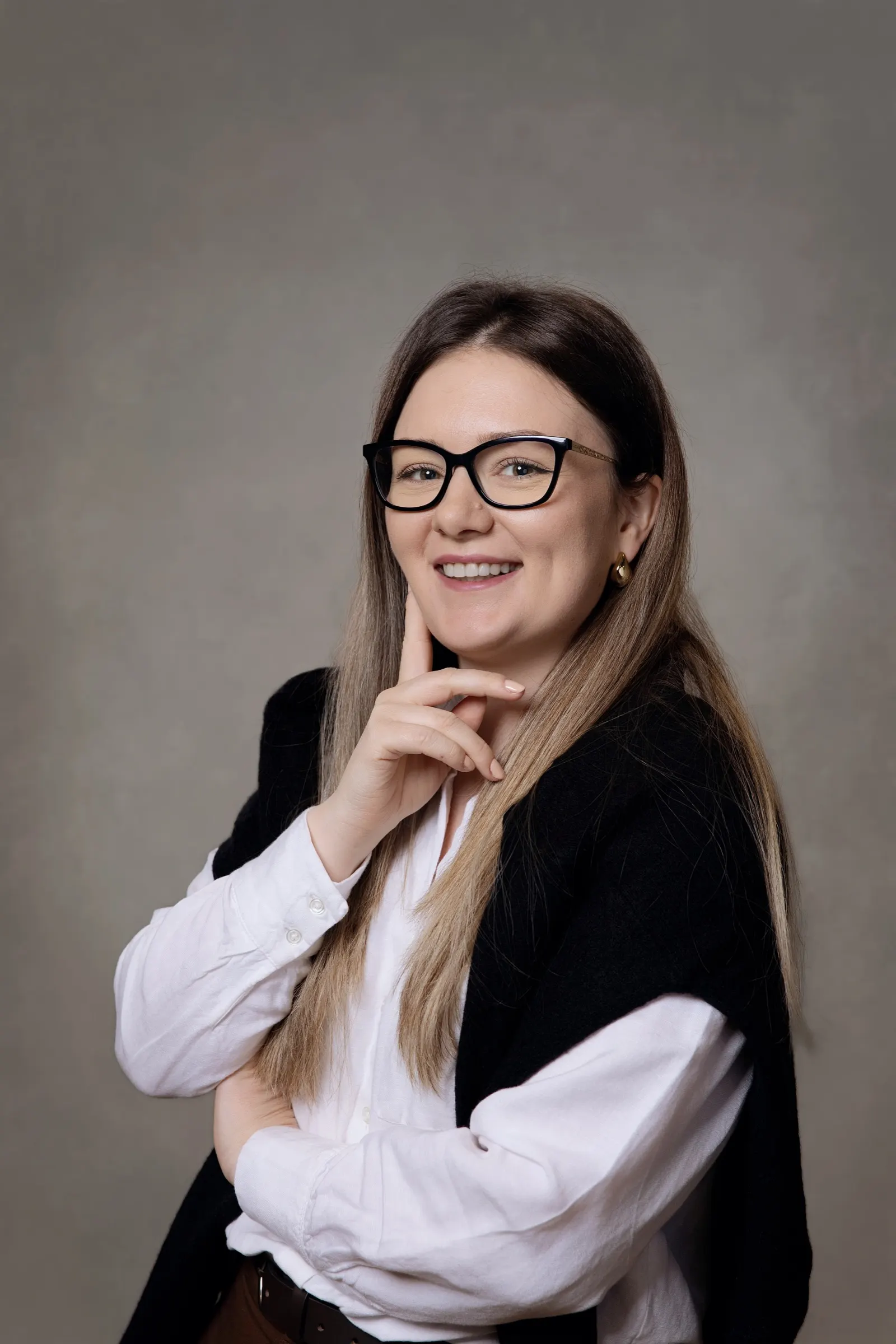 Retrato corporativo de una mujer con gafas y mano en la barbilla sobre fondo gris. Fotografía de Noomadik.