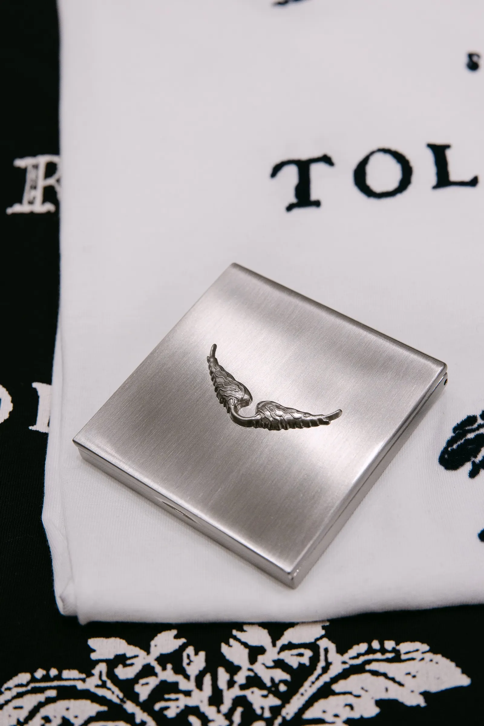 Caja metálica grabada con alas sobre una camiseta blanca en la presentación de Zadig & Voltaire. Fotografía de Noomadik.