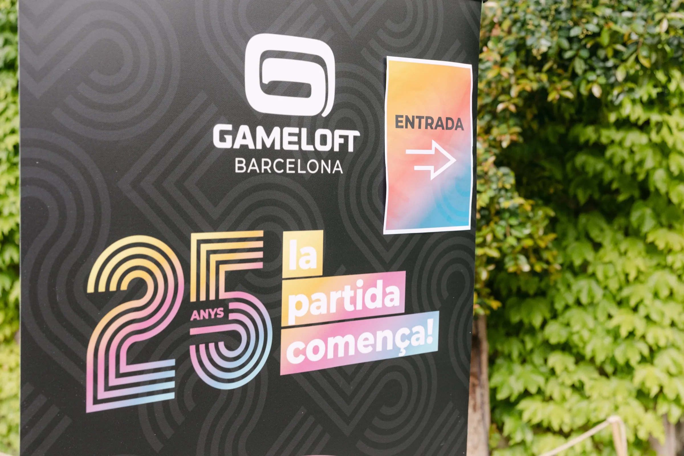 Cartel de entrada del 25 aniversario de Gameloft Barcelona junto a una pared de hiedra en Palo Alto. Fotografía de Noomadik.