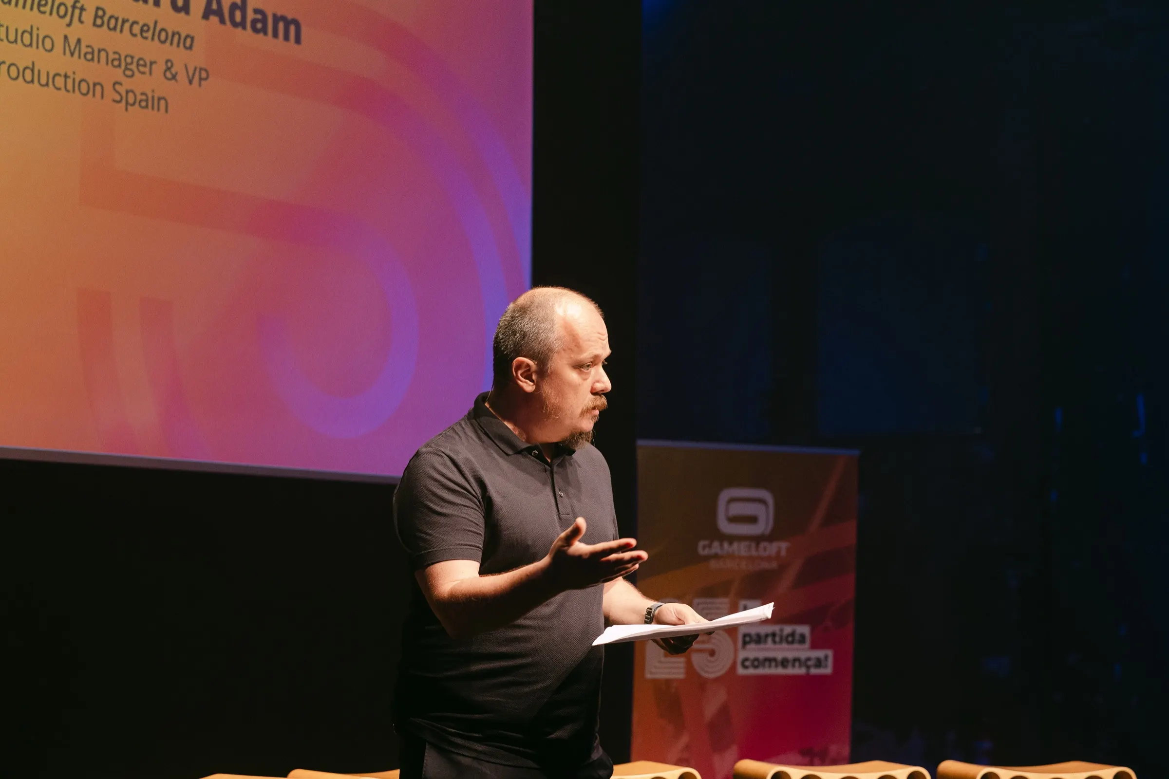 Ponente con papeles hablando en el escenario del 25 aniversario de Gameloft Barcelona. Fotografía de Noomadik.