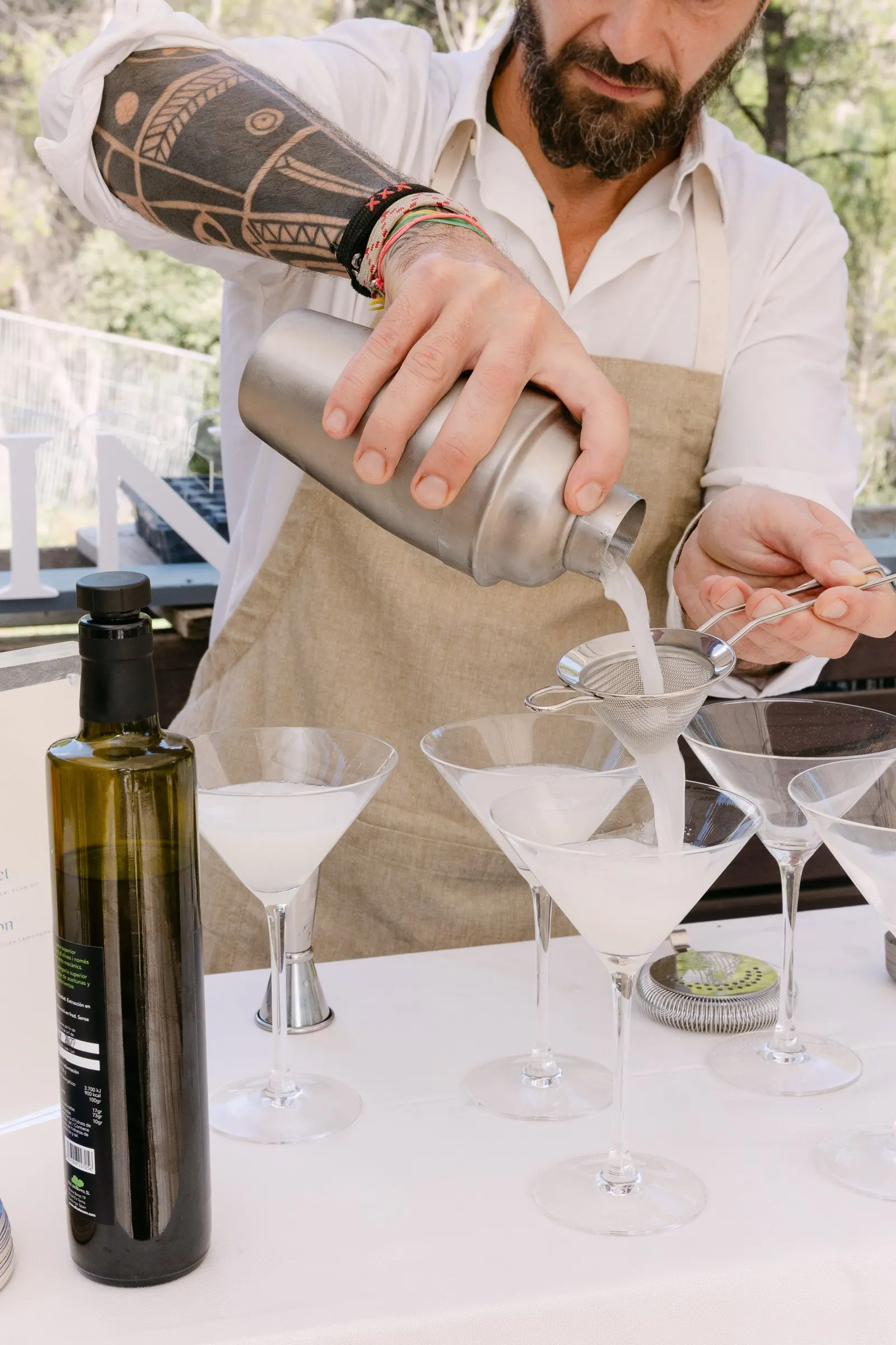 Bartender sirviendo cócteles en copas de martini junto a una botella de aceite. Fotografía de Noomadik.