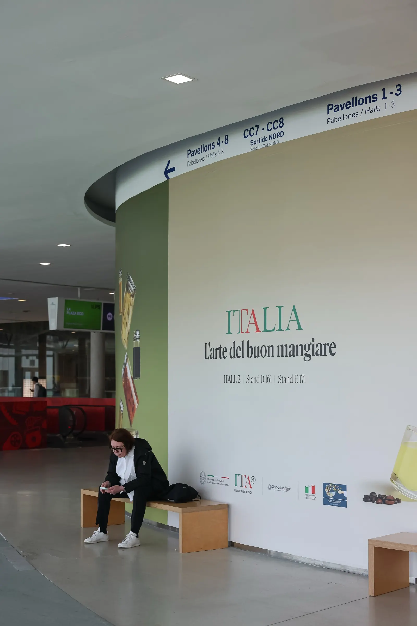 Pared señalizada del pabellón de Italia con una visitante sentada en un banco en Alimentaria. Fotografía de Noomadik.
