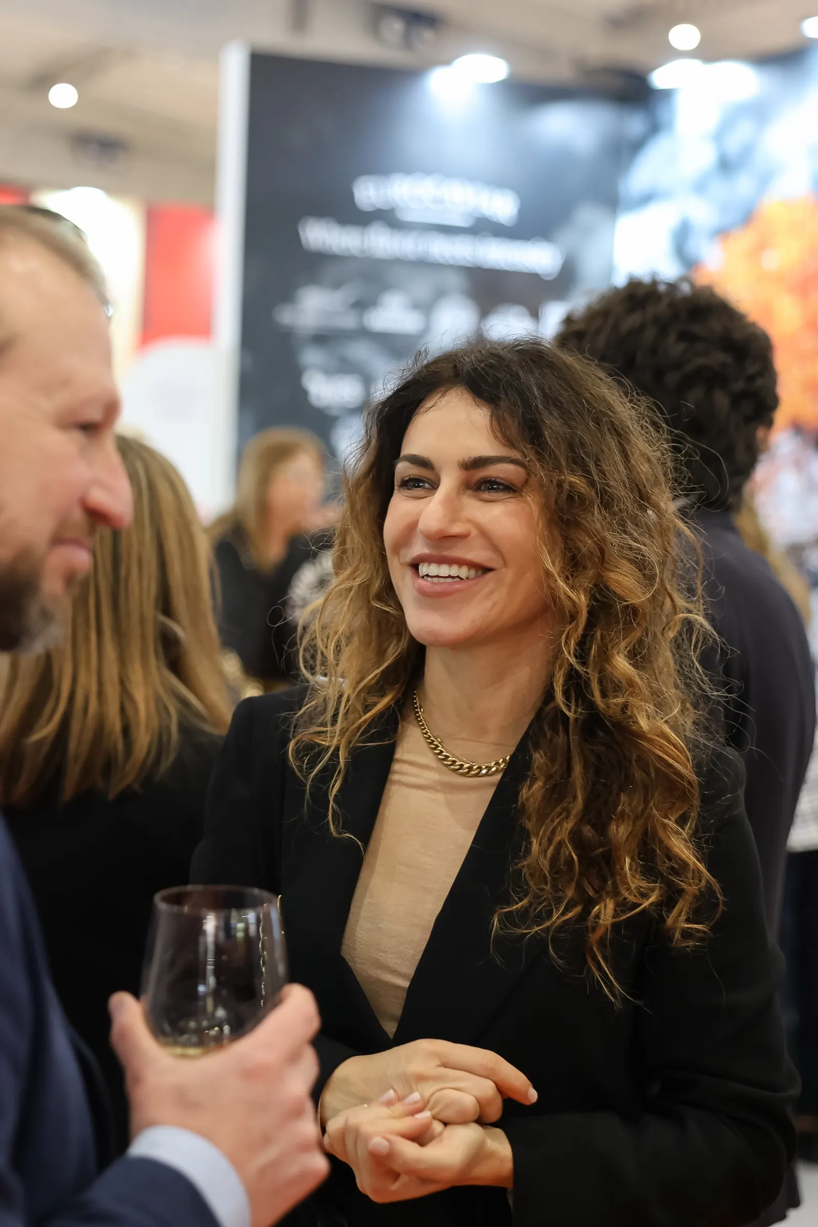 Invitada sonriente conversando con una copa en el pabellón de Italia en Alimentaria. Fotografía de Noomadik.