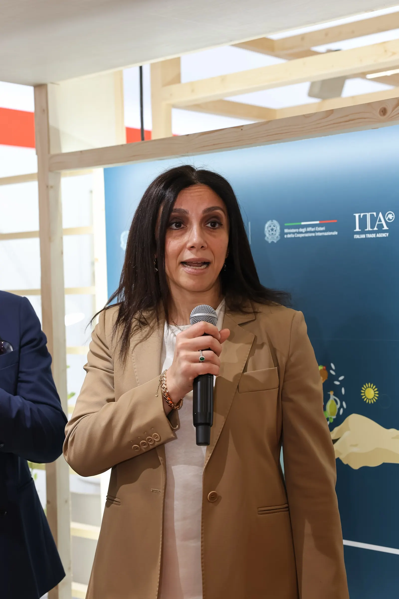 Ponente con micrófono durante la visita institucional al pabellón de Italia en Alimentaria. Fotografía de Noomadik.