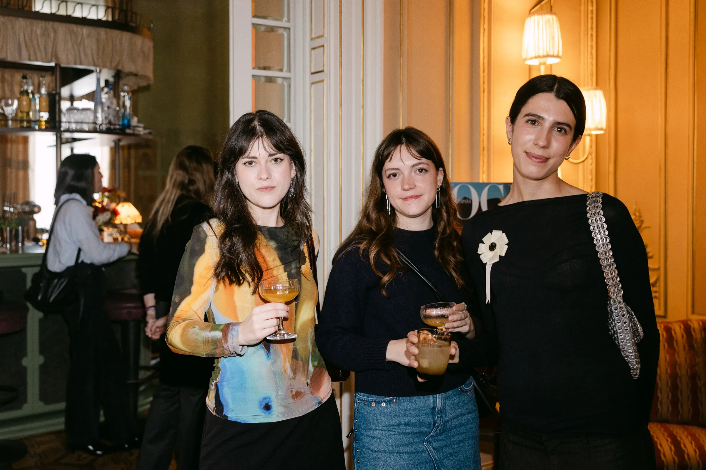 Tres invitadas con cóctel posan juntas en la presentación del número de Vogue España. Fotografía de Noomadik.