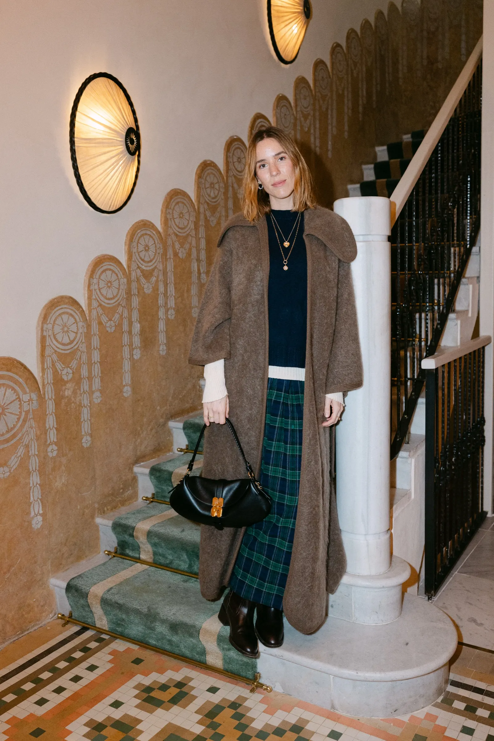 Invitada con abrigo largo posando en la escalera de Barcelona Pool House durante el encuentro de Vogue. Fotografía de Noomadik.