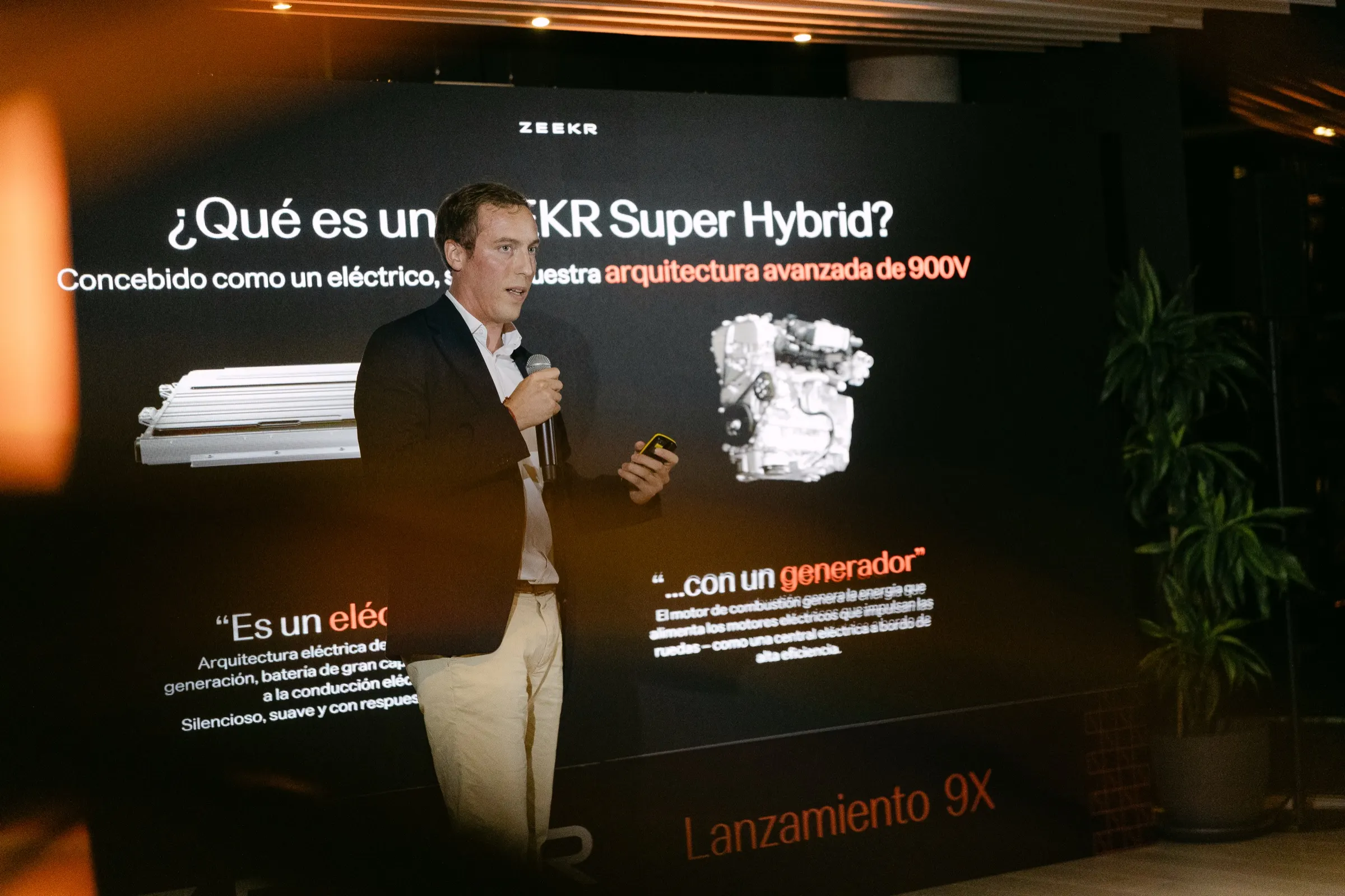 Portavoz con micrófono ante la pantalla que explica el sistema híbrido del Zeekr 9X. Fotografía de Noomadik.